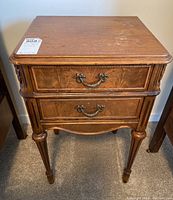 Front view of vintage wooden bed table showing two drawers with decorative metal handles and carved legs.