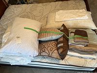 Queen size bed with bedding items including pillows, decorative covers, folded sheets, and a white duvet arranged on top.