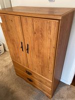 Front view of wood cabinet showing two paneled doors with black metal handles and two drawers with decorative pulls at the bottom.