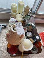 Overview showing arrangement of ceramic lamp, several pillar candles, glass and metal candle holders, and decorative accessories on a wooden table surface.