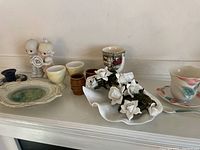 Overview of assorted ceramics including figurines, candle holder, egg cups, tea cup and saucer, porcelain flowers and jug.