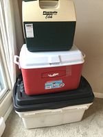 Stacked view of two coolers on top of two plastic storage containers of different sizes and colors.