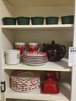 Photo of kitchen shelf showing green ramekins on upper shelf, red and white polka dot plates and saucers, brown teapot, and assorted mugs.
