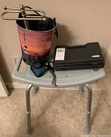 Photo of medical support stool with a decorative waste basket full of scissors and small tools and a black hard carrying case on the stool.