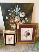 Photo showing three artworks: one large floral oil painting, two smaller framed floral prints or paintings.