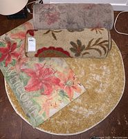 Four rugs displayed on floor including two rectangular door mats with floral designs and two runners, one round with floral pattern and one rolled solid color.