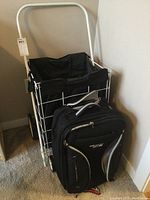 Photo showing full view of the metal-frame shopping trolley with black fabric basket and black wheeled carry on bag with gray and white accents.