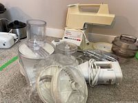 Overview of multiple small kitchen appliances parts including Phillips hand mixer, Oster kitchen center base, Black & Decker chopper parts, and miscellaneous attachments.