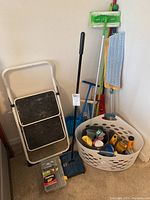 Photo showing folding step ladder next to cleaning tools and basket with supplies