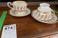 Two tea cups and two matching saucers displayed on a wooden surface with one cup upside down showing rim detail.
