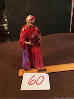 Photo shows ceramic figurine of woman holding a pot, with a purple vase beside her and a ruler for scale.
