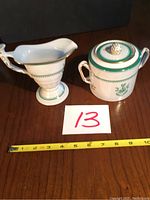 Photo showing a creamer and a sugar bowl with lid from Spode's Newburyport Collection, with a measuring tape indicating size and a label with the number 13.