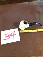Angle view showing pipe with carved bowl and black stem, alongside measurement tape and lot number card