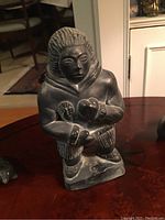 Front view of an Inuit carved figure depicting a person in traditional clothing holding an object.