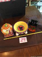 Full view showing all three Halloween-themed decorative items including pumpkin candy dish, Halloween candle holder, and jack-o-lantern candle holder with measuring tape for scale.