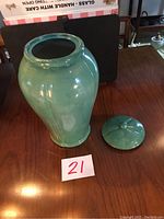 Light green pottery vase with round removable lid placed beside it on a wooden surface, white glazed interior visible at vase opening.