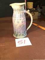 Side view of hand thrown pottery pitcher with pink and blue glaze, showing spout and handle.