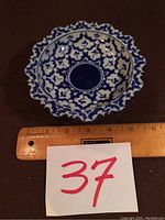Photo of a white and blue raised candy dish showing scalloped edges and intricate floral pattern with a ruler indicating it is approximately 5 inches wide.