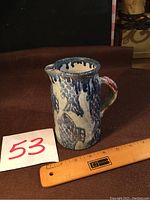 Front view of small ceramic pitcher with blue fish pattern, showing decorative blue drip glaze near top, and reddish tint on handle.