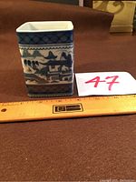 Side view of the small blue and white square container next to a ruler for size reference showing height around 3.5 inches.