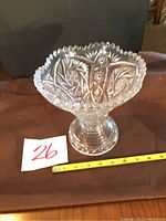 Front side view of clear cut glass vase showing intricate floral and geometric patterns, scalloped rim, and pedestal base with measuring tape indicating size.
