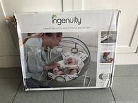 Front of the box showing the product image of the automatic baby bouncer by Ingenuity with a baby and mother interacting.