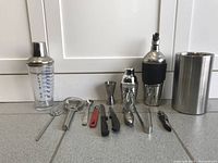 Photo showing full bar set with cocktail shakers, ice bucket, and assorted bartending tools laid out on a kitchen counter.