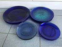Four blue glass plates displayed on a tiled floor showing size and variety in color and pattern