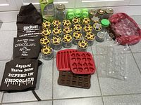 Lot contents showing aprons, glass jars with decorative lids, plastic containers, and silicone chocolate molds.