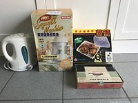 Front view of all four items: Mizda Hot Soymilk Machine in box, Williamsburg Food Warmer box, white electric kettle, microwave steamer box.