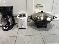 Three appliances: Black & Decker coffee maker, white Proctor Silex toaster, and stainless steel electric wok with lid and temperature control base.
