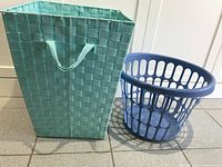 Two laundry baskets side by side on tile floor. One is tall and rectangular in light blue woven plastic. The other is round and blue plastic with open side holes.