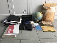 Overview of office supplies lot laid out on floor showing globe, binders, papers, envelopes, and holders