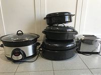 Full view of Crock Pot, stacked black roasting pots with lids, and stainless steel toaster on kitchen countertop.