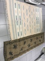 Two rugs side by side: a beige southwestern style area rug with blue and gray geometric designs and a long palm tree design runner rug in light brown with dark olive green palm trees and border patterns.