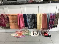 Photo shows multiple scarves draped over a counter including patterned and solid color scarves along with packages of hosiery arranged underneath.