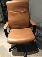 Front view of tan faux leather high back office chair with padded seat, armrests, and wheel base.
