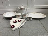 Full view of porcelain serving set including coffee pot, creamer, sugar bowl, serving platter, vegetable bowl, salt and pepper shakers, and knitted coffee pot warmer.