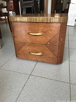 Front view of vintage wooden end table showing two drawers with brass handles and veneer finish. Visible wear and scratches on surface.
