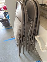 Side view showing four stacked folding chairs with brown metal frames and beige cushioned seats and backs.