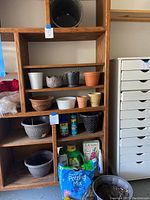 Shelf unit with various ceramic, terracotta, woven, and plastic pots as well as garden care products including bagged potting mix and sprays