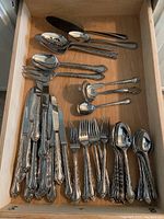 Photo showing entire silverware collection in drawer with multiple forks, spoons, knives, and serving utensils laid out with handle details