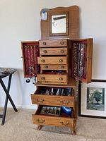 Front view of wood jewelry box with drawers and side doors open revealing hooks and felt lining.