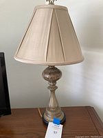 Full view of the table lamp showing the beige fabric shade and metal base with marble details, placed on a wooden surface.