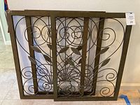 Three metal wall panels arranged against a wall showing intricate leaf and scroll metal design within rectangular frames.