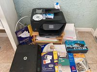 Photo showing HP OfficeJet all-in-one printer on shelf with business card packs, white paper, and HP portable scanner on floor.