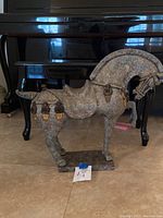 Side view of the stone horse sculpture showing detailed harness and belt-like straps with ornamental elements and patina.