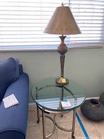 Full view of the round glass-top table with metal legs and the decorative metal lamp placed on top, showing placement and scale.