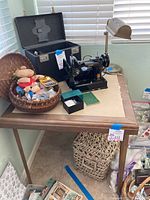 Photo of vintage wooden card table with soft beige top and collapsible legs. Metal adjustable lamp with beige lampshade beside it. Other items on table not included.