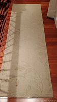 Full length photo of the wool area rug on hardwood floor showing light beige color and leaf motif pattern.